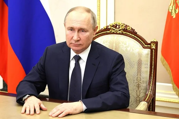 Владимир Путин за рабочим столом на фоне флага России; в отношении него Международный уголовный суд выдал ордер за депортацию украинских детей.